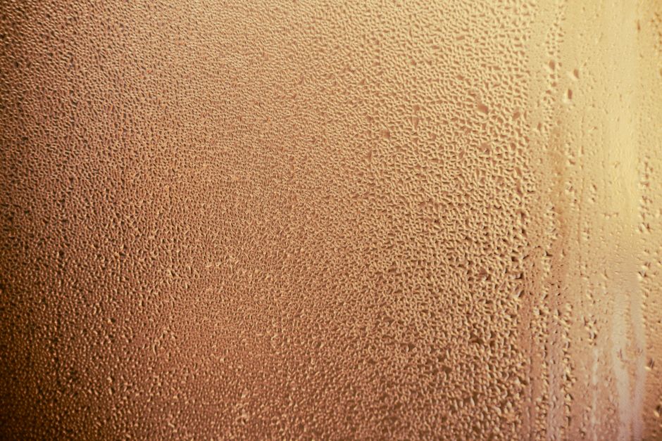 A detailed shot of dewdrops creating a pattern on a glass surface with warm lighting.